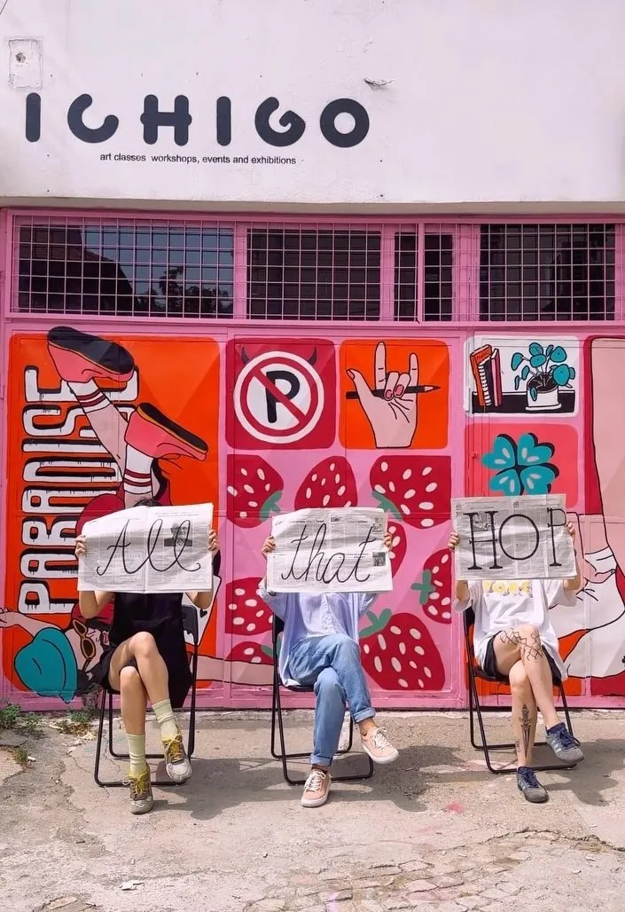 Trei oameni cu ziare pe care scrie „All that HOP”, în fața ușii pictate